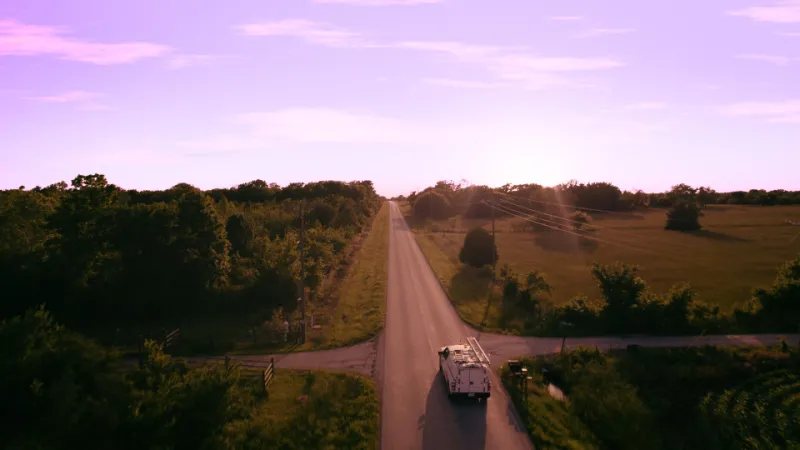 A utility truck driving into the sunset on an empty country road 